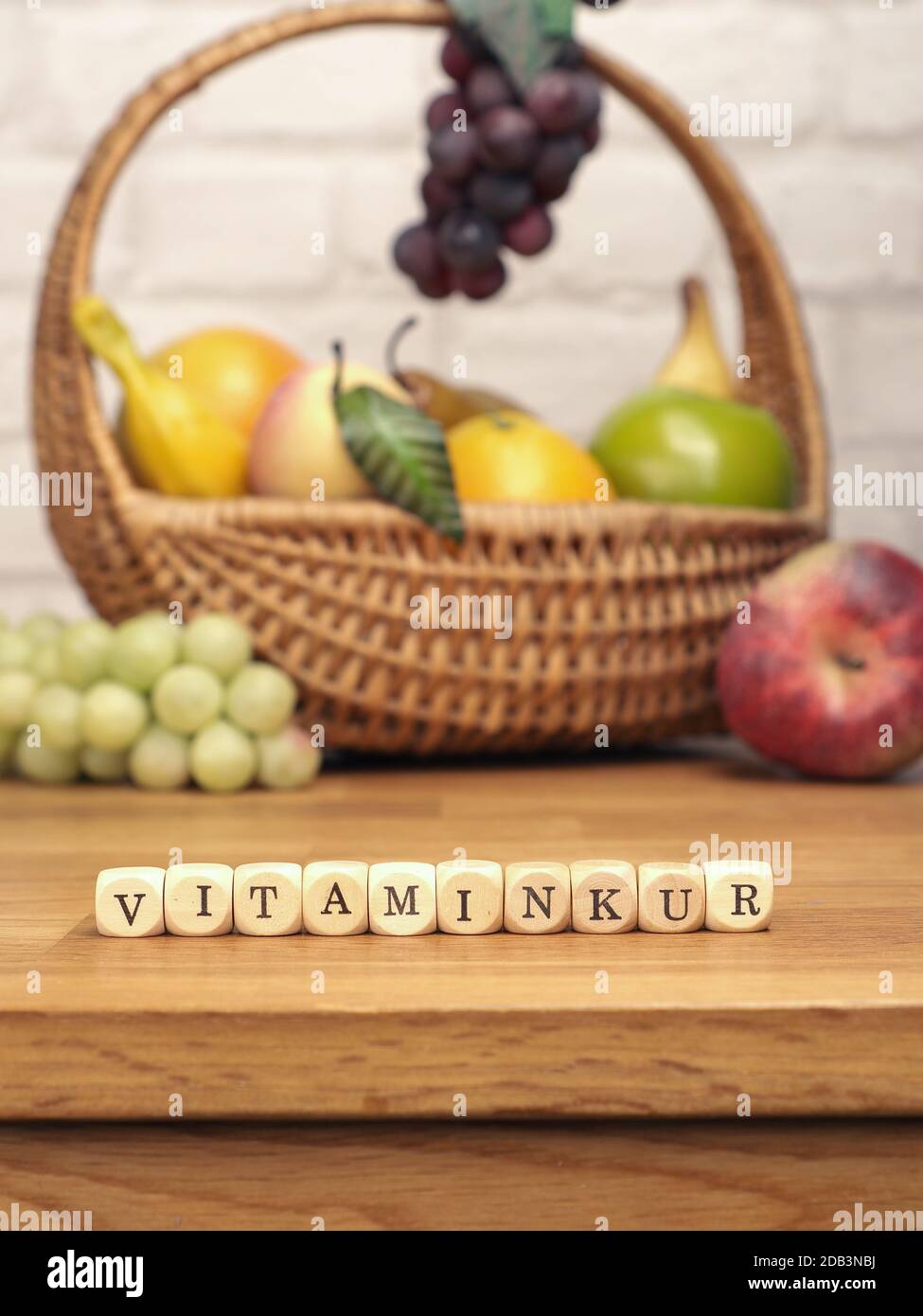 Piccoli blocchi di legno con la parola tedesca Vitamin cura su un tavolo da cucina con frutta fresca sullo sfondo, concetto di cibo sano Foto Stock