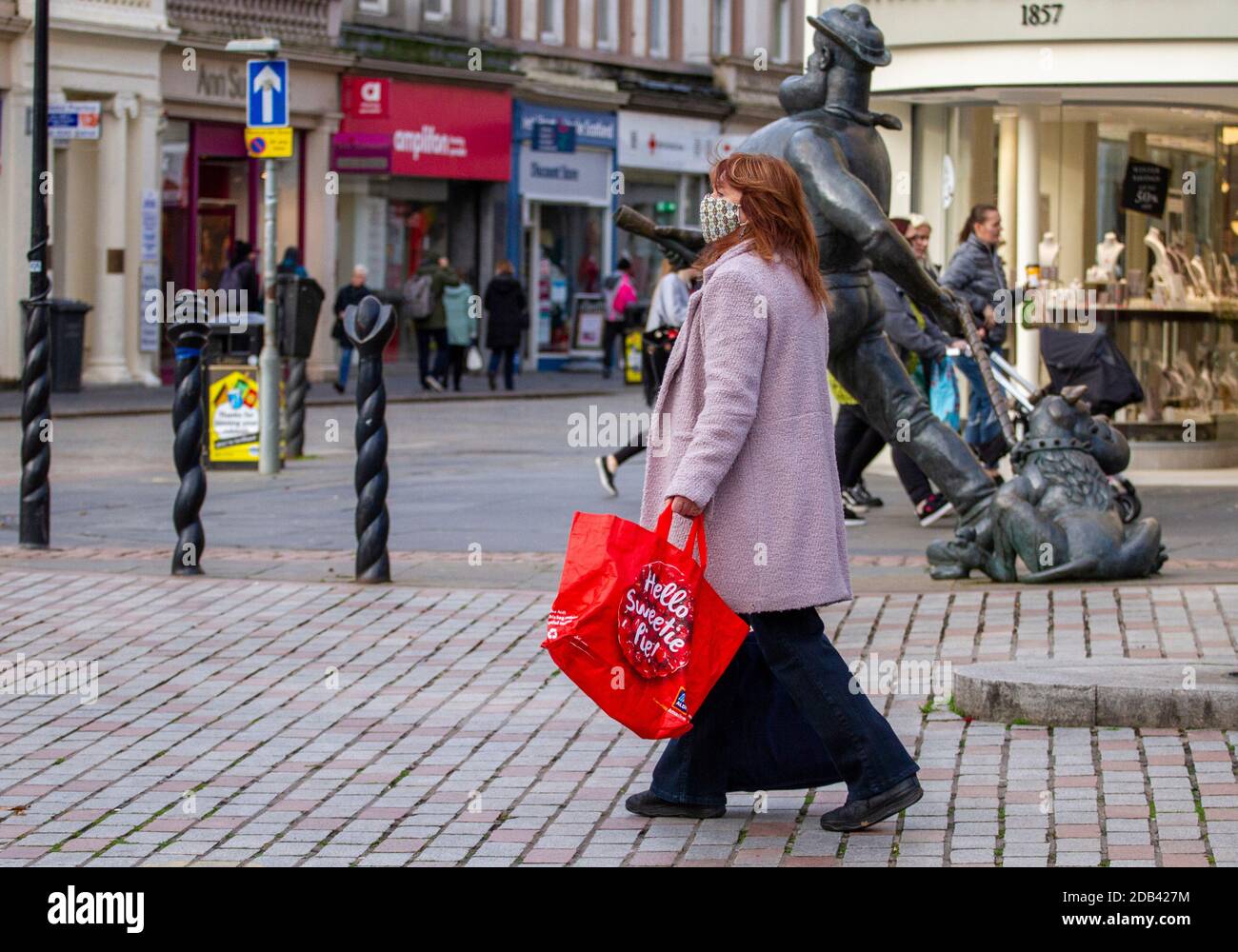 Dundee, Tayside, Scozia, Regno Unito. 16 Nov 2020. Notizie del Regno Unito Covid-19 Lockdown. Le persone che camminano per le strade di Dundee con pochi negozi di abbigliamento essenziali aperti dal livello 3 più rigoroso Covid-19 Lockdown restrizione è stato imposto. Una donna alla moda è consapevole delle linee guida per le distanze sociali e l'uso di maschere facciali a piedi, mentre si tiene in mano una grande borsa portavalatte "Hello Sweetie Pie" Aldi durante il suo shopping di Natale in centro città in un freddo e soleggiato pomeriggio di novembre. Credit: Dundee Photographics/Alamy Live News Foto Stock