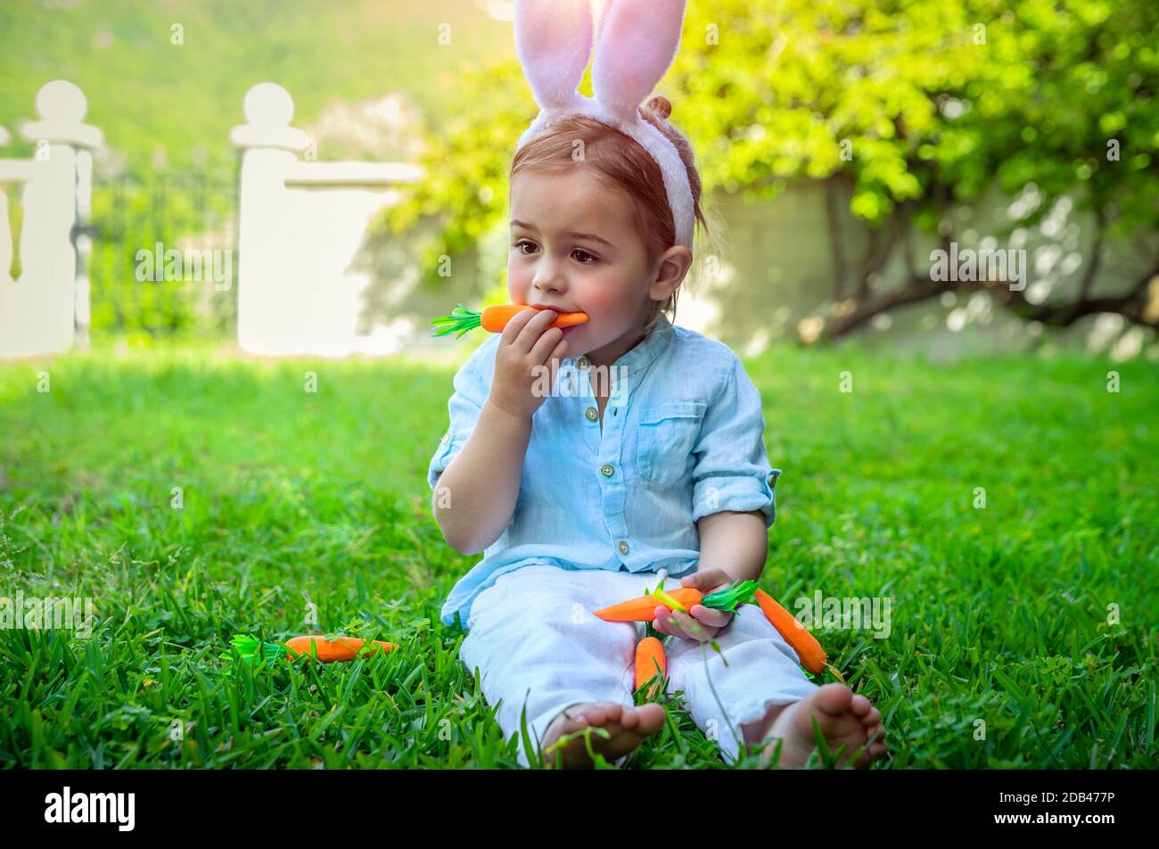 Carino ragazzo vestito come un coniglietto, il bambino che mangia carote, felice vacanza cristiana, tradizionale vestito di Pasqua, il bambino godere di primavera all'aperto Foto Stock