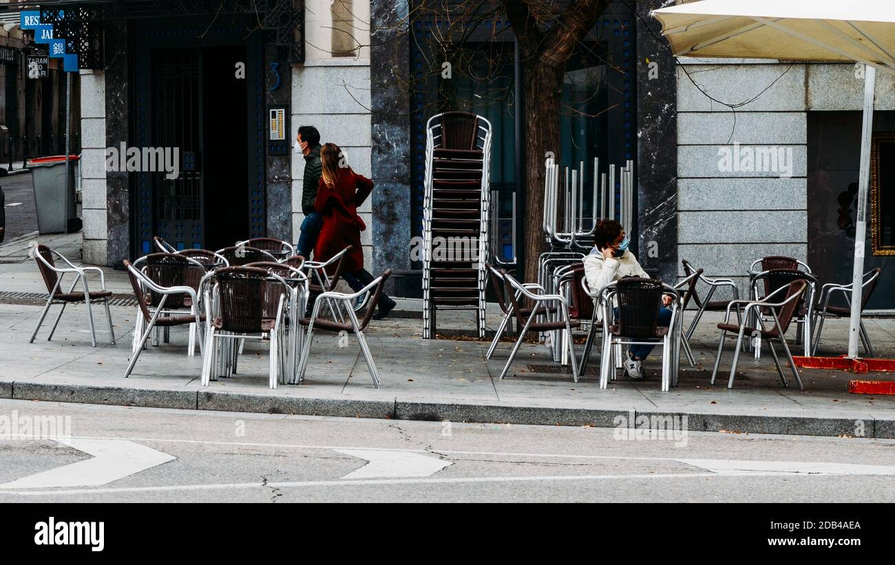 La donna si siede da sola su sedie e tavoli vuoti socialmente distanziati fuori da un caffè nel centro di Madrid, Spagna Foto Stock