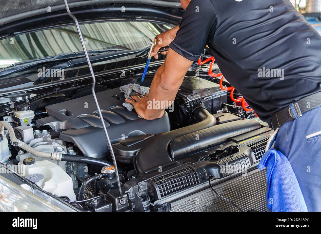 Il meccanico controlla il motore.l'uomo che tiene le mani pulisce il motore.il meccanico utilizza una pistola ad aria compressa per pulire il motore. Foto Stock