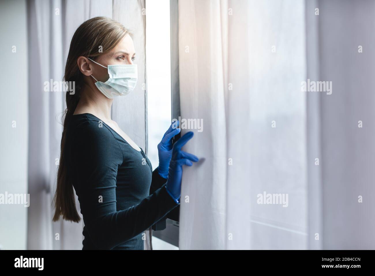 Annoiata donna in quarantena corona che guarda fuori dalla finestra per la strada Foto Stock