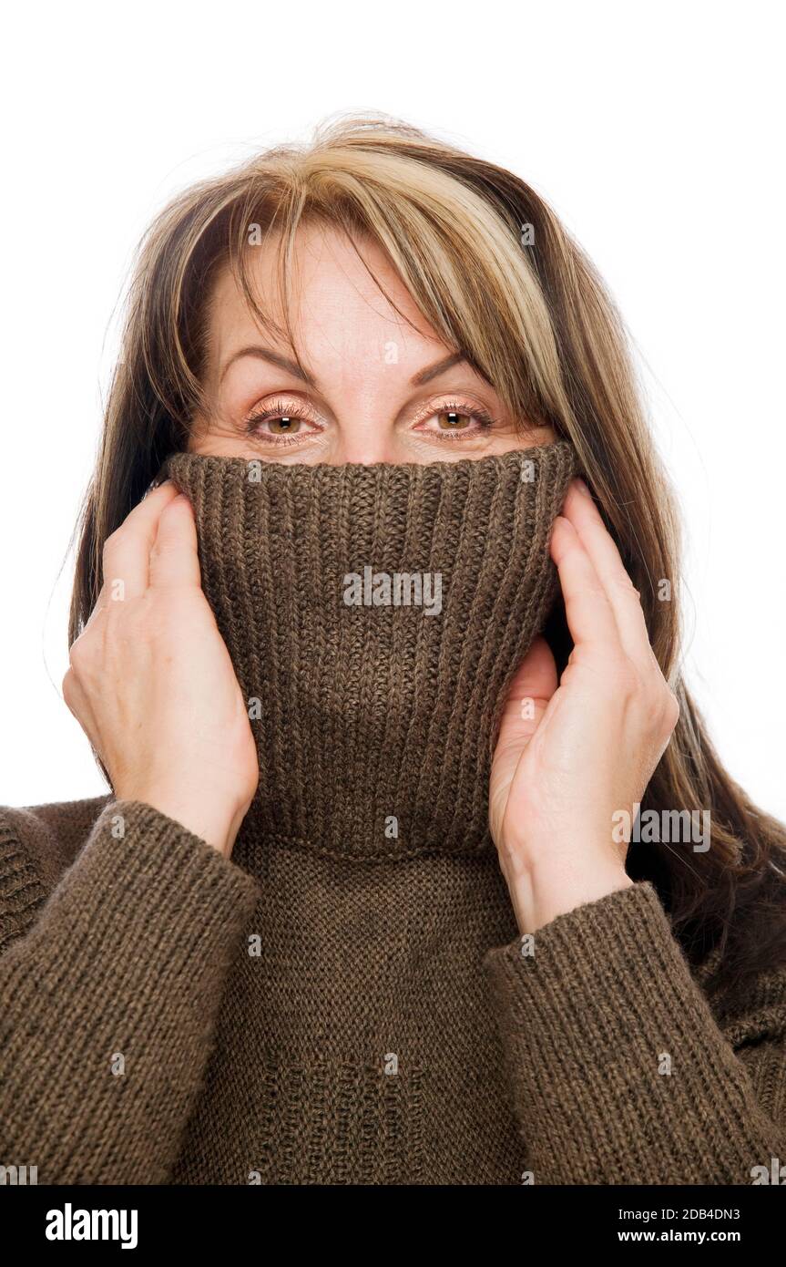 Vista frontale di una donna di mezza età con un pullover marrone a turleneck tirato sopra il naso su uno sfondo bianco. Foto Stock