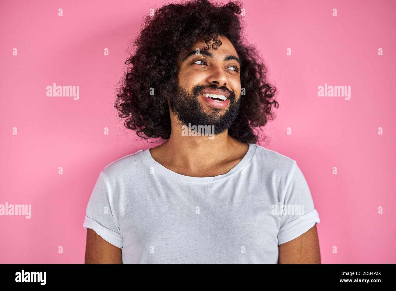 ritratto di allegro positivo maschio di aspetto arabico guardando via ridendo, ascolta scherzo, divertirsi con qualcuno, isolato su sfondo rosa Foto Stock