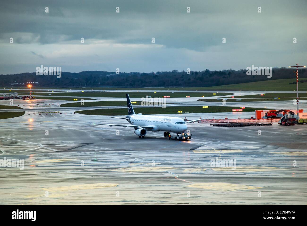 Lufthansa Aircraft sulla Taxiway in aeroporto la sera nuvolosa dopo la pioggia, visto dal terminal Foto Stock