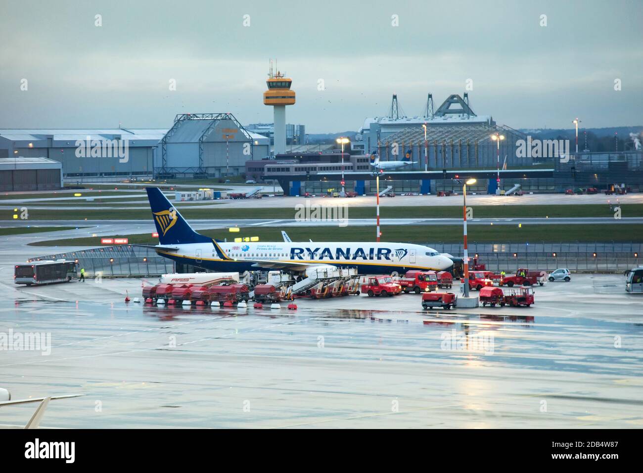 Ryanair Aircraft per la manutenzione della linea di taxi nell'aeroporto di Amburgo, tra i veicoli di servizio. Vista dalla finestra terminale in un giorno nuvoloso dopo la pioggia Foto Stock