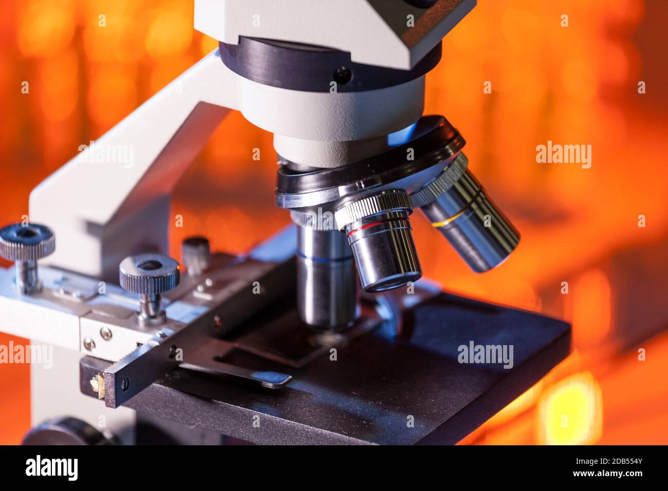 Primo piano delle lenti per microscopio focalizzate su un campione in una  luce arancione calda. Matraccio da laboratorio sullo sfondo Foto stock -  Alamy