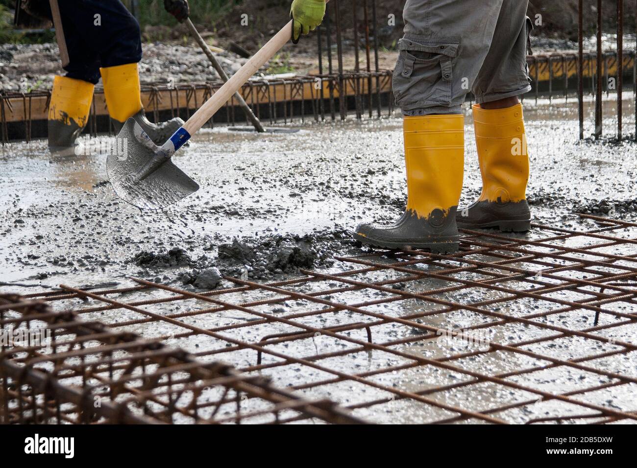 due muratori al lavoro su un cantiere durante la posa di calcestruzzo per costruire le fondamenta di una casa Foto Stock