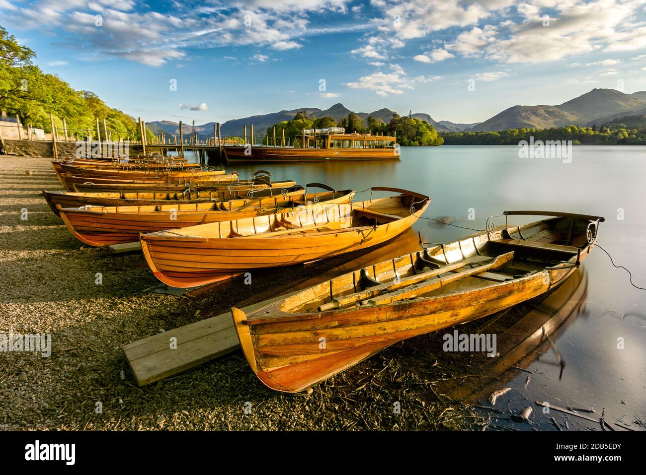 Barche di canottaggio in legno allineate sulla costa che sono illuminate con luce dorata dal sole che tramonta. Derwentwater, Lake District, Regno Unito. Foto Stock