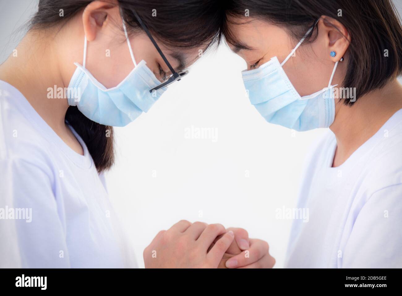 Due donne madre e figlia indossare una maschera per prevenire l'epidemia di coronavirus con una sensazione triste, testa contro l'altro tenere le mani per conforto encorour Foto Stock