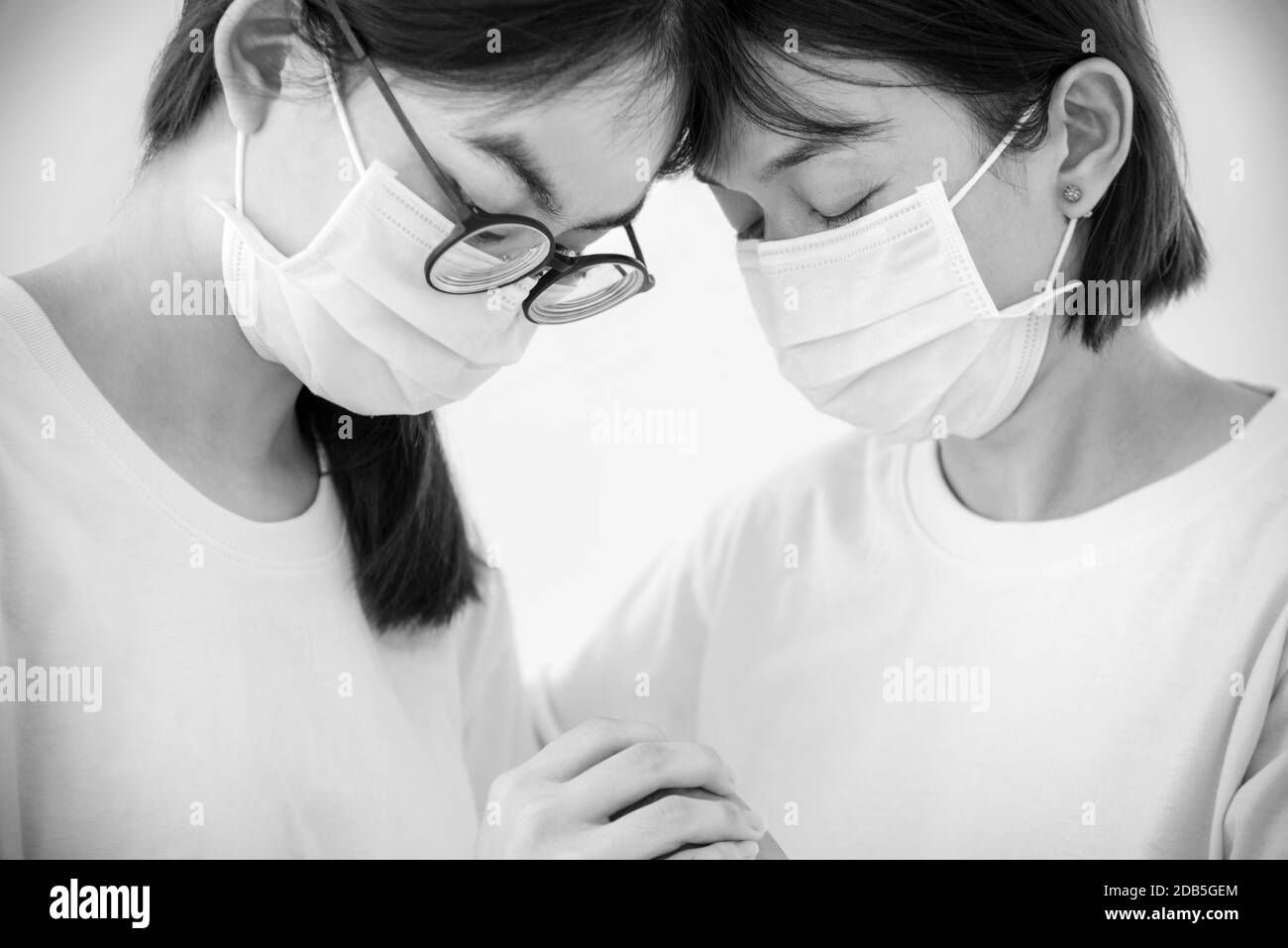 Due donne madre e figlia indossare una maschera per prevenire l'epidemia di coronavirus con una sensazione triste, testa contro l'altro tenere le mani per conforto encorour Foto Stock