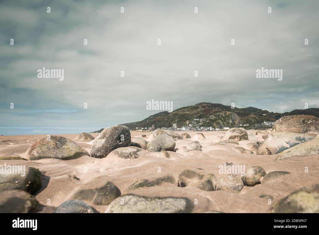 Riprese ad angolo basso attraverso le rocce costiere e la sabbia che guardano verso Barmouth Bay nel Galles del Nord, Regno Unito Foto Stock