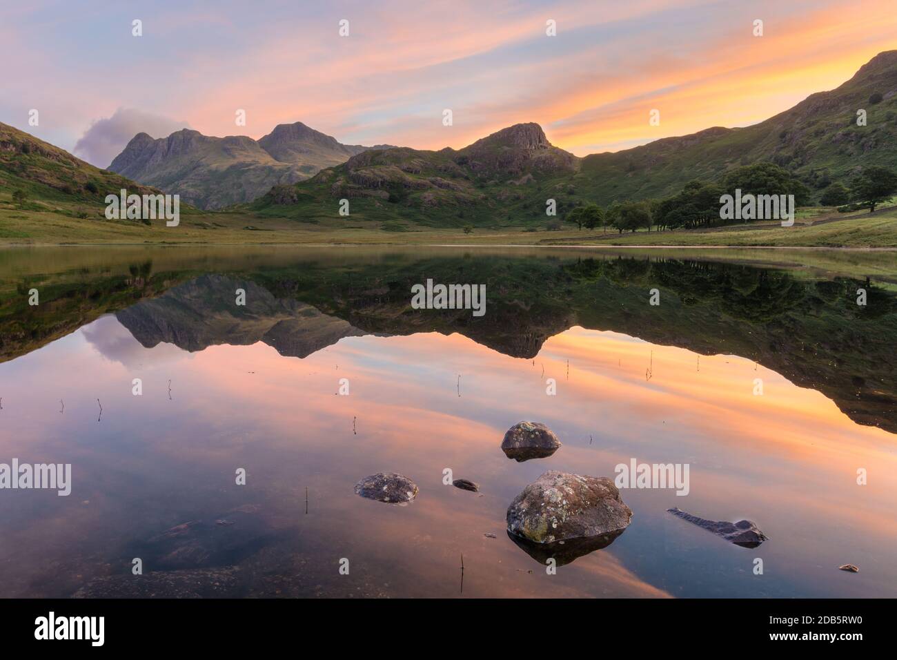 Alba vibrante con idilliaci riflessi specchiati in lago con rocce. Blea Tarn, Lake District, Regno Unito. Foto Stock