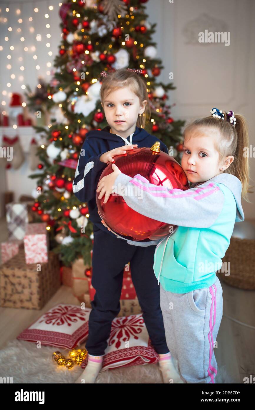 Una bambina sta tenendo una grande sfera di vetro rossa per l'albero di Natale. Natale, anno nuovo, decorazioni per le vacanze a casa, famiglia, preparazione Foto Stock