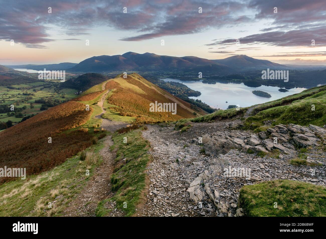 Sentiero roccioso sulle Catbells in autunno mattina con luce solare che colpisce la montagna e l'alba vibrante. Foto Stock