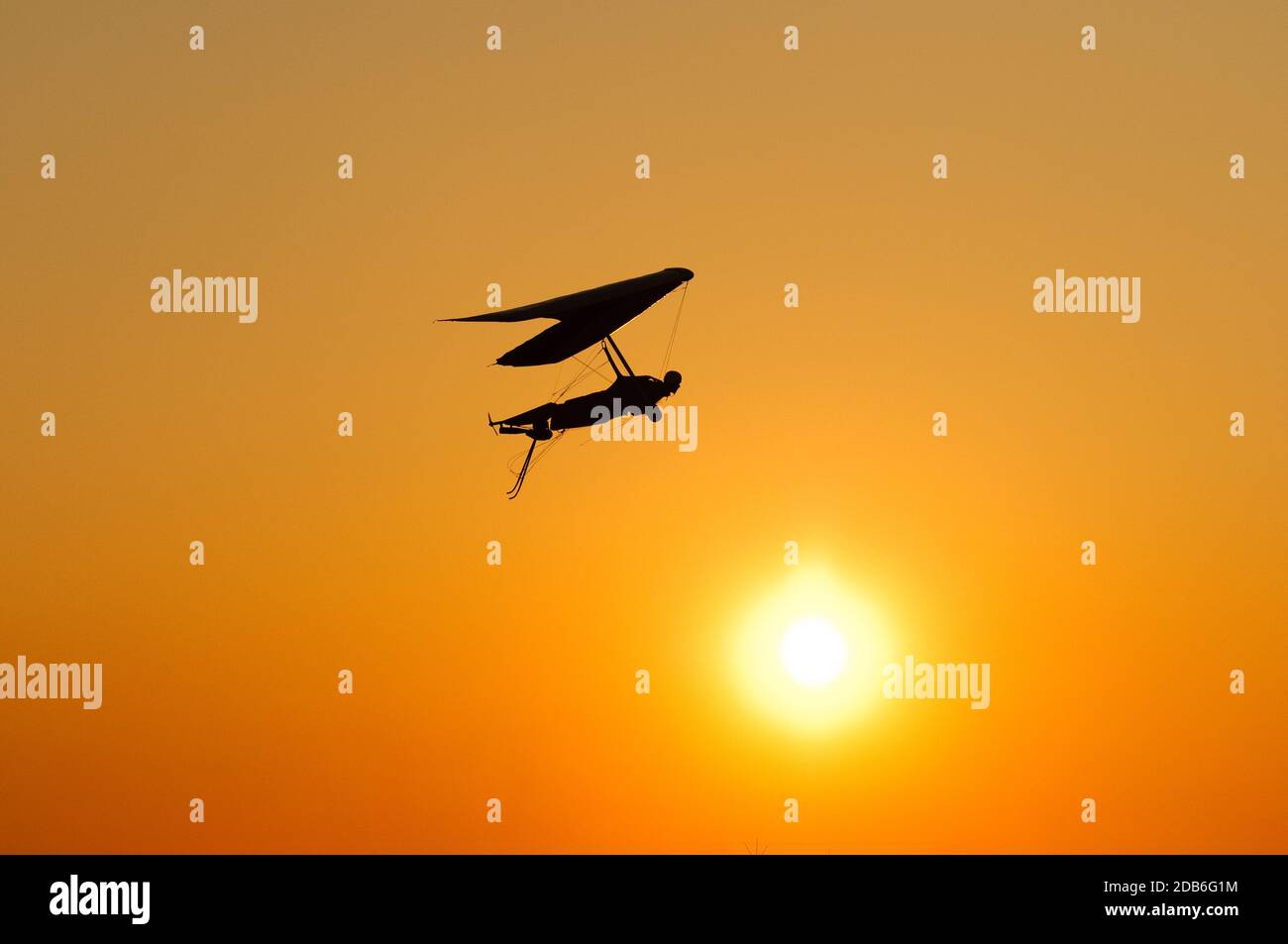 La silhouette dell'ala deltaplano si appende al sole brillante del tramonto. Sogno di volare come un uccello Foto Stock