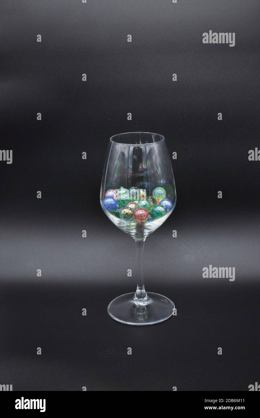 bicchiere di vino riempito con marmi di vetro colorati e collana di perle Foto Stock