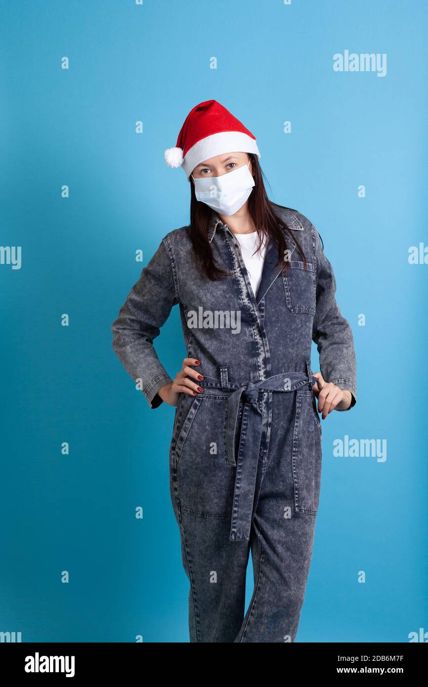 Ritratto a tutta lunghezza di donna asiatica che indossa cappello di Santa e maschera medica protettiva sul viso, isolato su sfondo blu Foto Stock