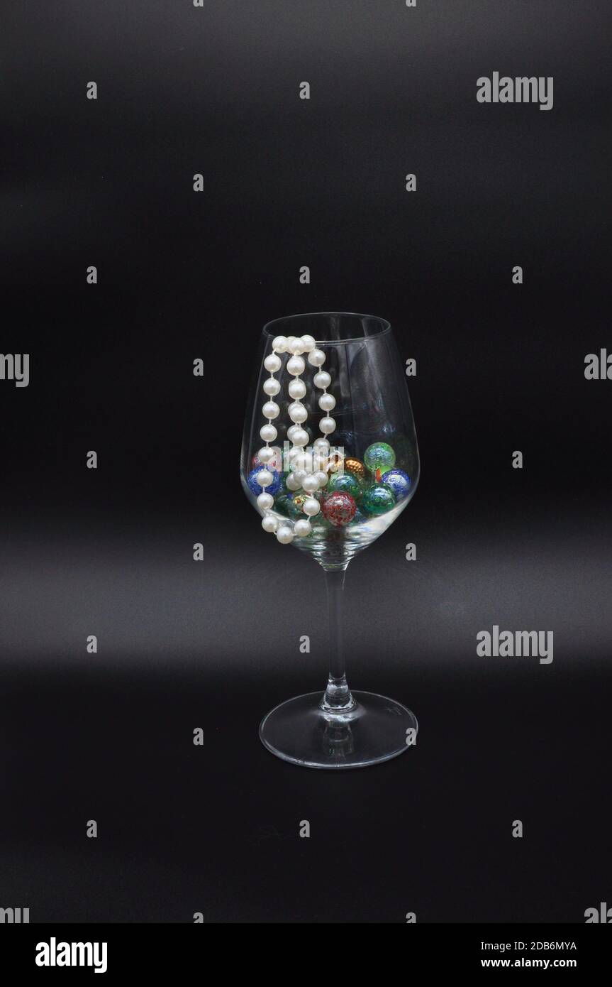 bicchiere di vino riempito con marmi di vetro colorati e collana di perle Foto Stock