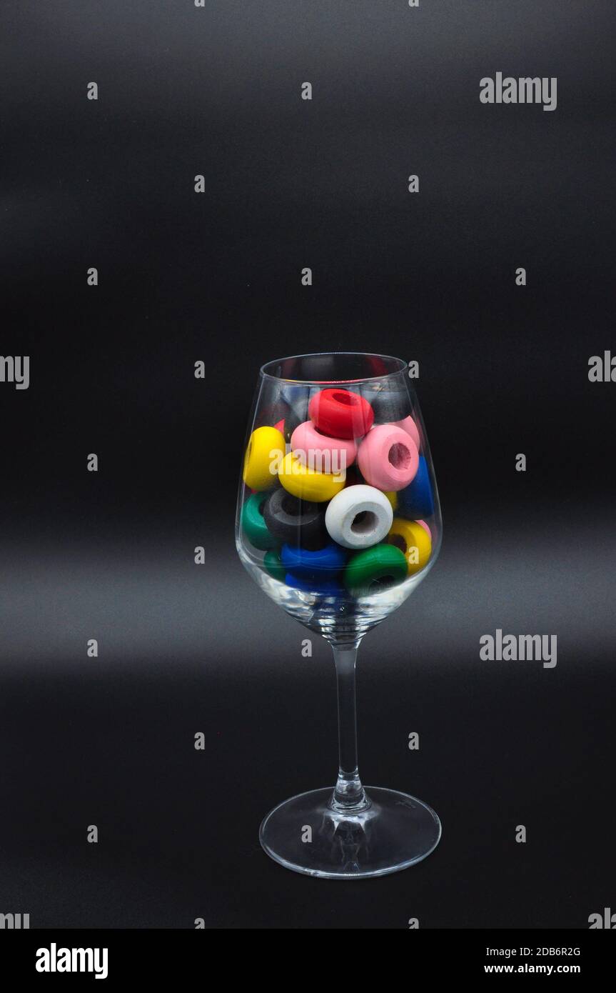 Bicchiere di vino riempito con cerchi di legno di molti colori su sfondo nero Foto Stock