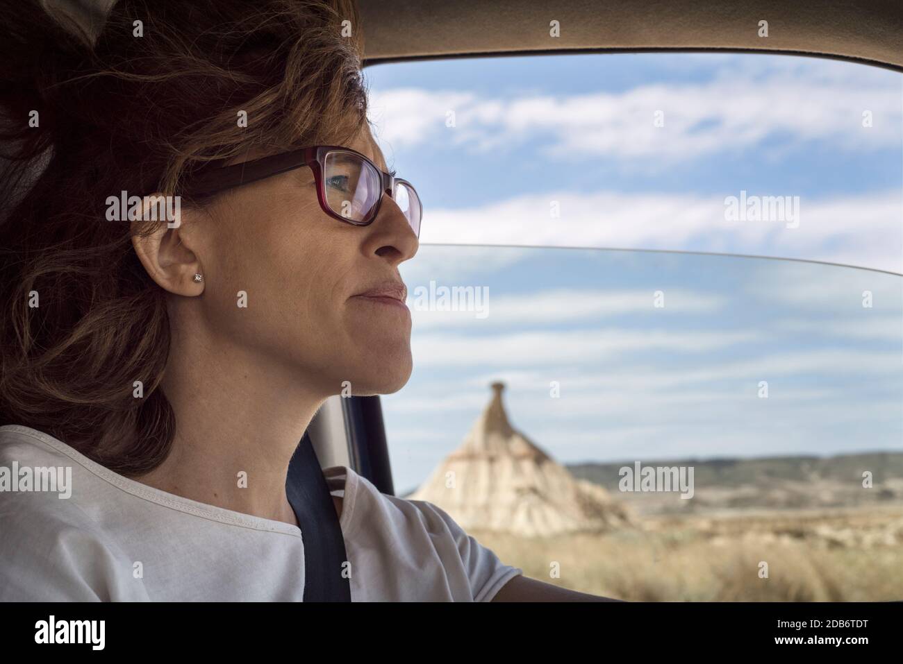 Donna che guida auto attraverso il Parco Naturale Bardenas Reales, Navarra, Spagna Foto Stock