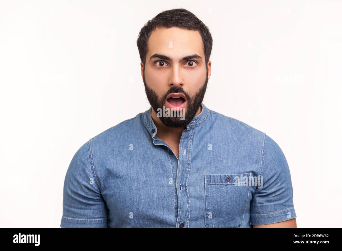 Sorpreso uomo meravigliato con barba in camicia blu guardando la macchina fotografica con occhi grandi e bocca aperta, scioccato con notizie inaspettate. Studio interno girato isola Foto Stock