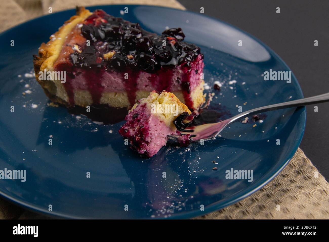 Fette di torta mousse di mirtillo con riflessi frutti di bosco decorati e foglie di menta su una piastra blu sono su tavola nera, primo piano. Viste dall'alto. Foto Stock