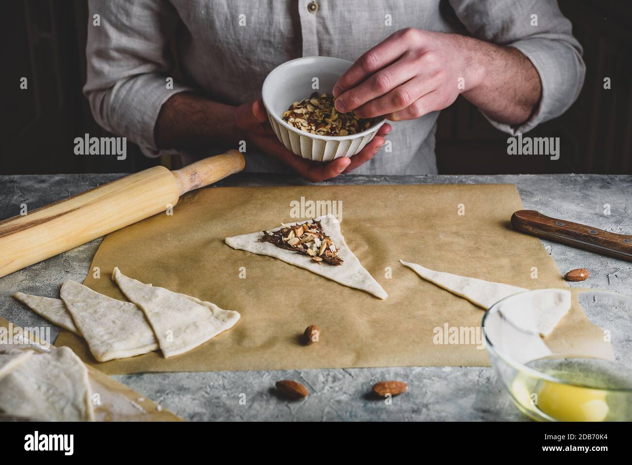 Preparazione di croissant. Baker spolverò le mandorle tritate sopra la nocciola spalmata Foto Stock