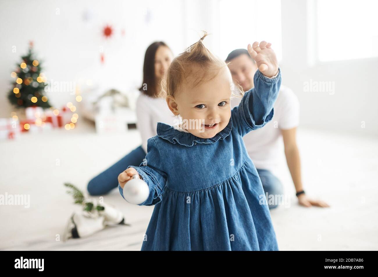 Ritratto di una bambina vestita con un abito in denim blu in piedi in una stanza luminosa. Foto Stock