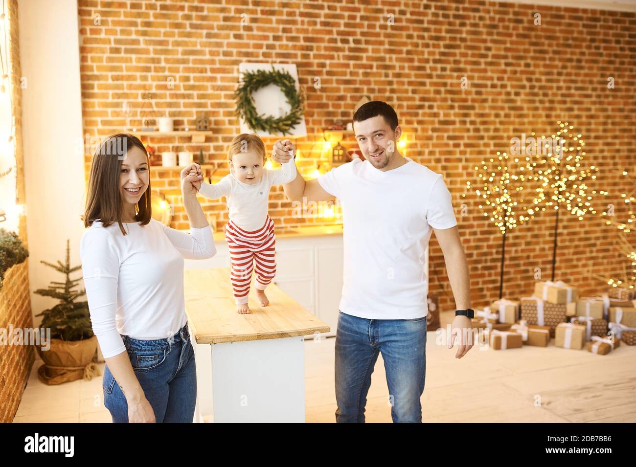 Una giovane famiglia con un bambino piccolo che si diverte a Natale a casa in una stanza accogliente e luminosa. Foto Stock