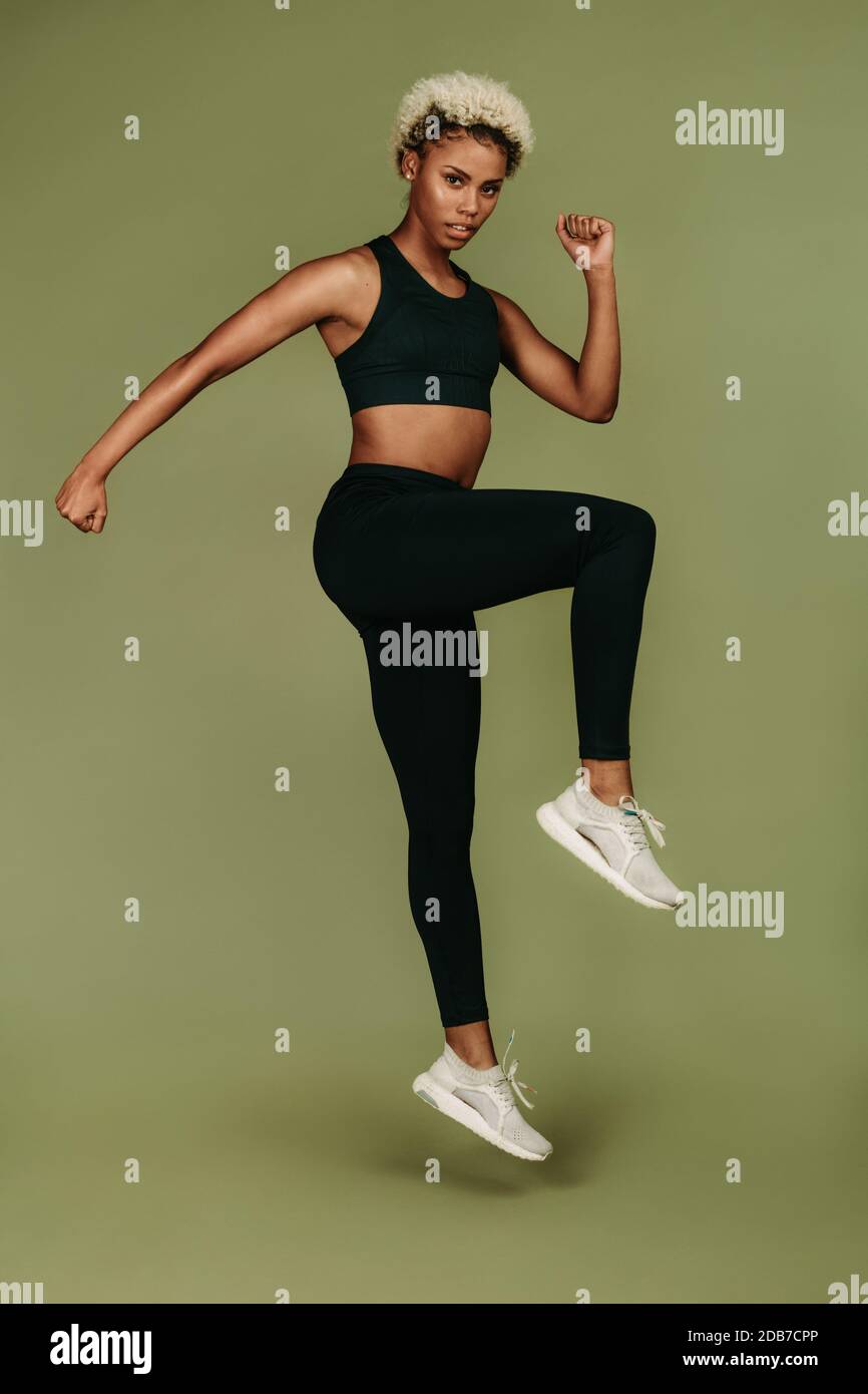 Atleta femminile afro-americana che fa esercizi di riscaldamento. Donna in forma fisica indossare fuori su sfondo verde. Foto Stock