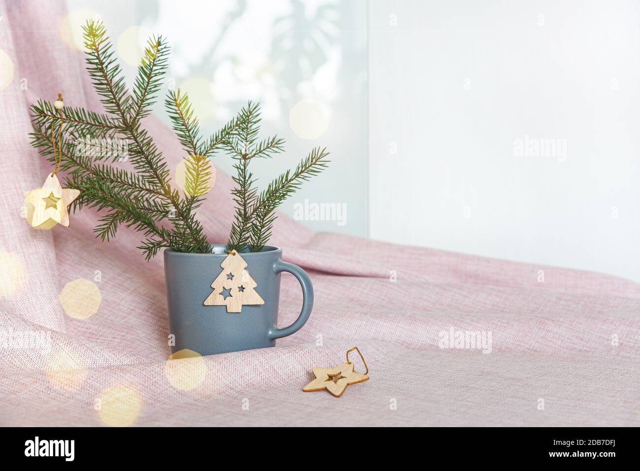 Ramo di abete con decorazioni in legno natalizio in una tazza di ceramica grigia su un panno rosa. Bokeh d'oro. Home decorazione concetto per le vacanze invernali. Foto Stock