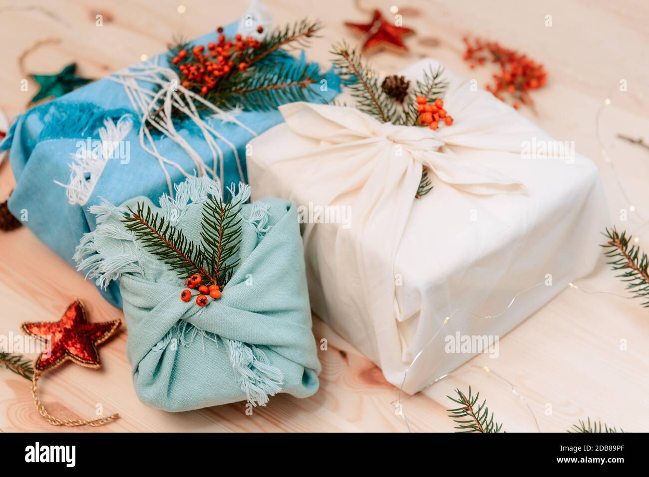 Zero rifiuti natale concetto. Scatole regalo avvolte in tessuto con ramificazione di abete rosso e bacche su sfondo di legno. Piatto. Eco-compatibile sostenibile Foto Stock