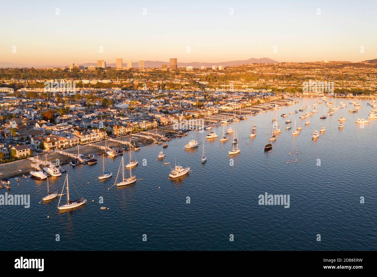Vista aerea delle barche ancorate a Newport Beach Harbour con Balboa Island e il lontano skyline in oro bagliore di tramonto Foto Stock