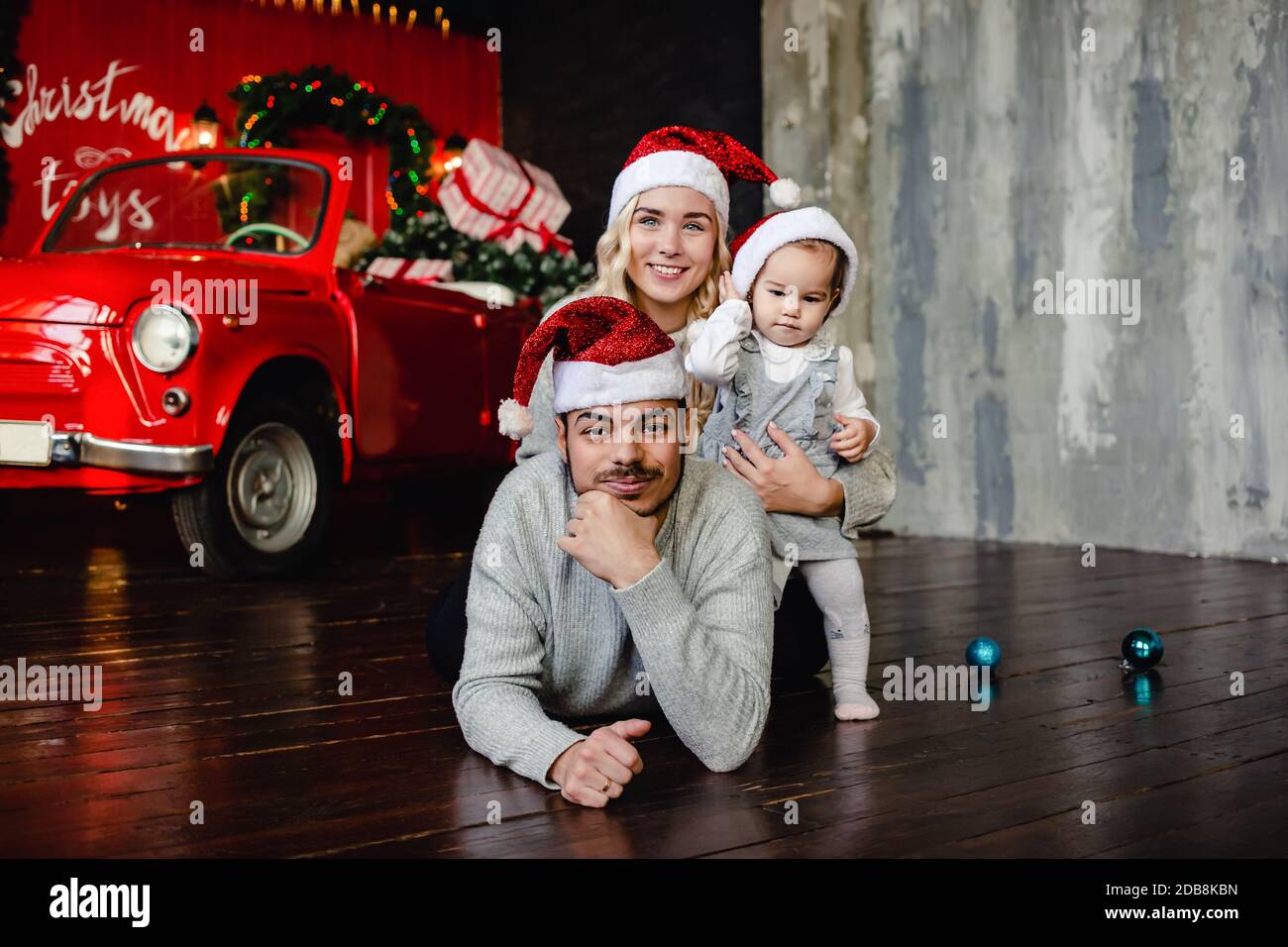 Genitori allegri con la figlia su cappello di Santa a casa con sfondo di Natale. Genitore e bambino piccolo che si diverte. Buon Natale e buone feste Foto Stock