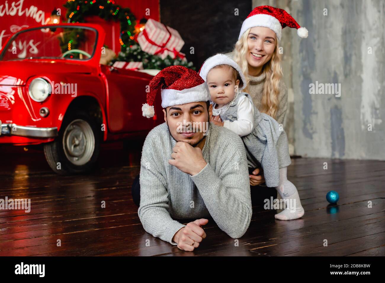 Genitori allegri con la figlia su cappello di Santa a casa con sfondo di Natale. Genitore e bambino piccolo che si diverte. Buon Natale e buone feste Foto Stock