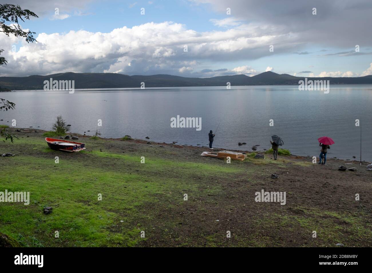 Due persone che guardano una persona che pesca sotto la pioggia, Lago di Bracciano, Lazio, Italia Foto Stock