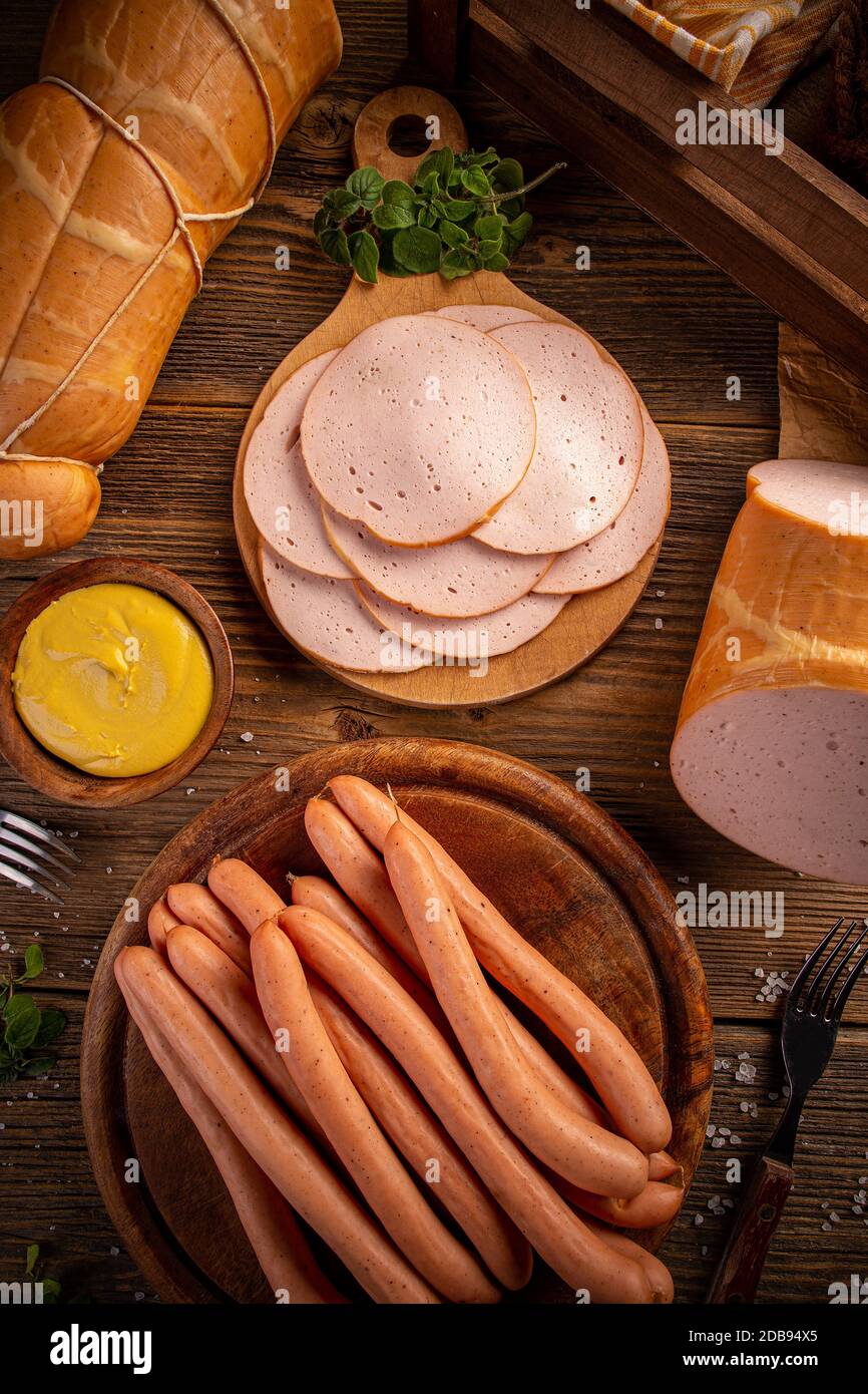 Salsicce e salumi bolliti freschi serviti con senape su tagliere in legno Foto Stock