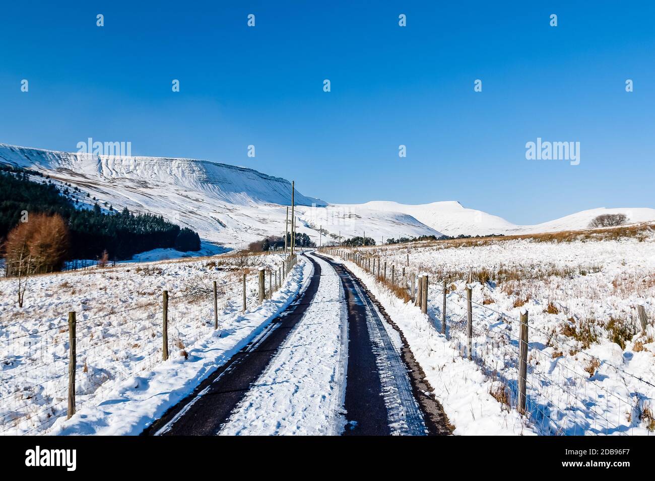 Una strada stretta che conduce alle montagne innevate in una giornata luminosa e soleggiata in inverno Foto Stock