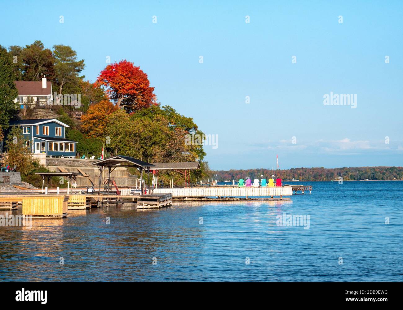 Lago tranquillo dove un pontile bianco con sedie colorate si estende verso l'esterno. Cottage paesaggio sul fiume San Lorenzo di Ontario, Canada. Foto Stock