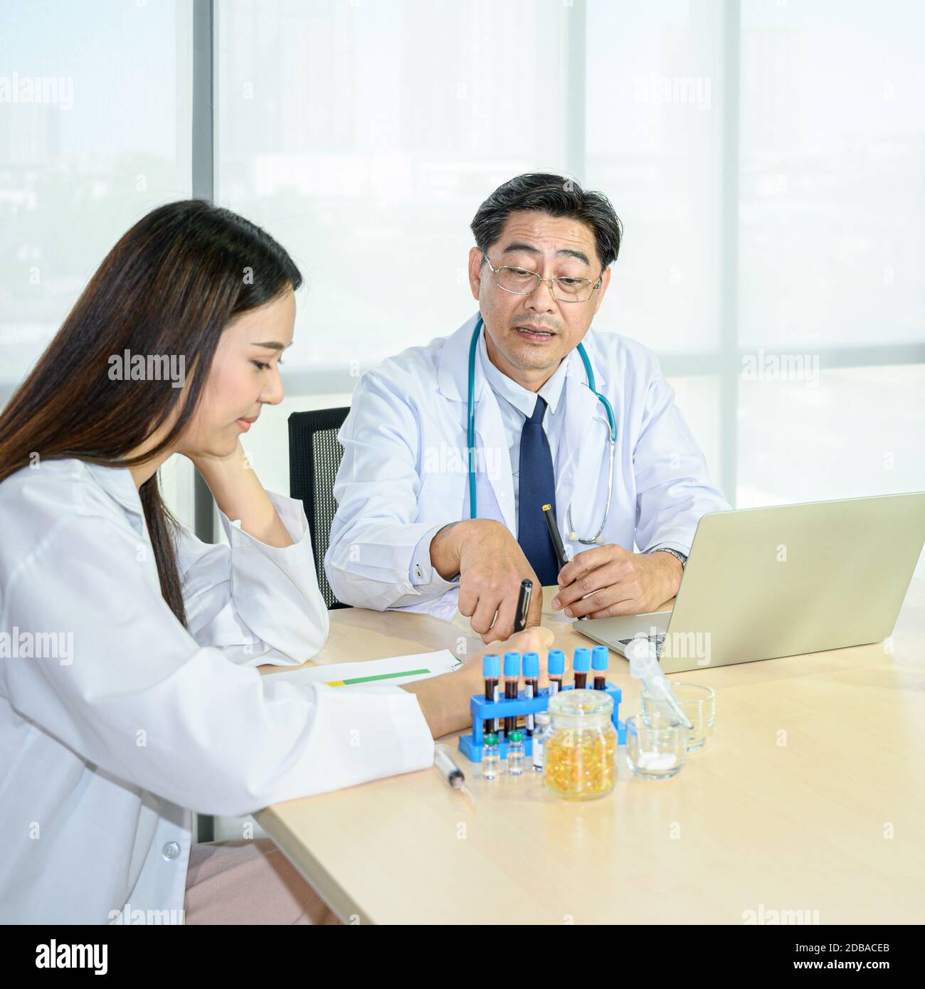Coppia di medico maschile asiatico adulto e femminile asiatica giovane medico che indossa formale cappotto bianco lavoro di squadra brainstorm incontro con il computer computer portatile all'hos Foto Stock
