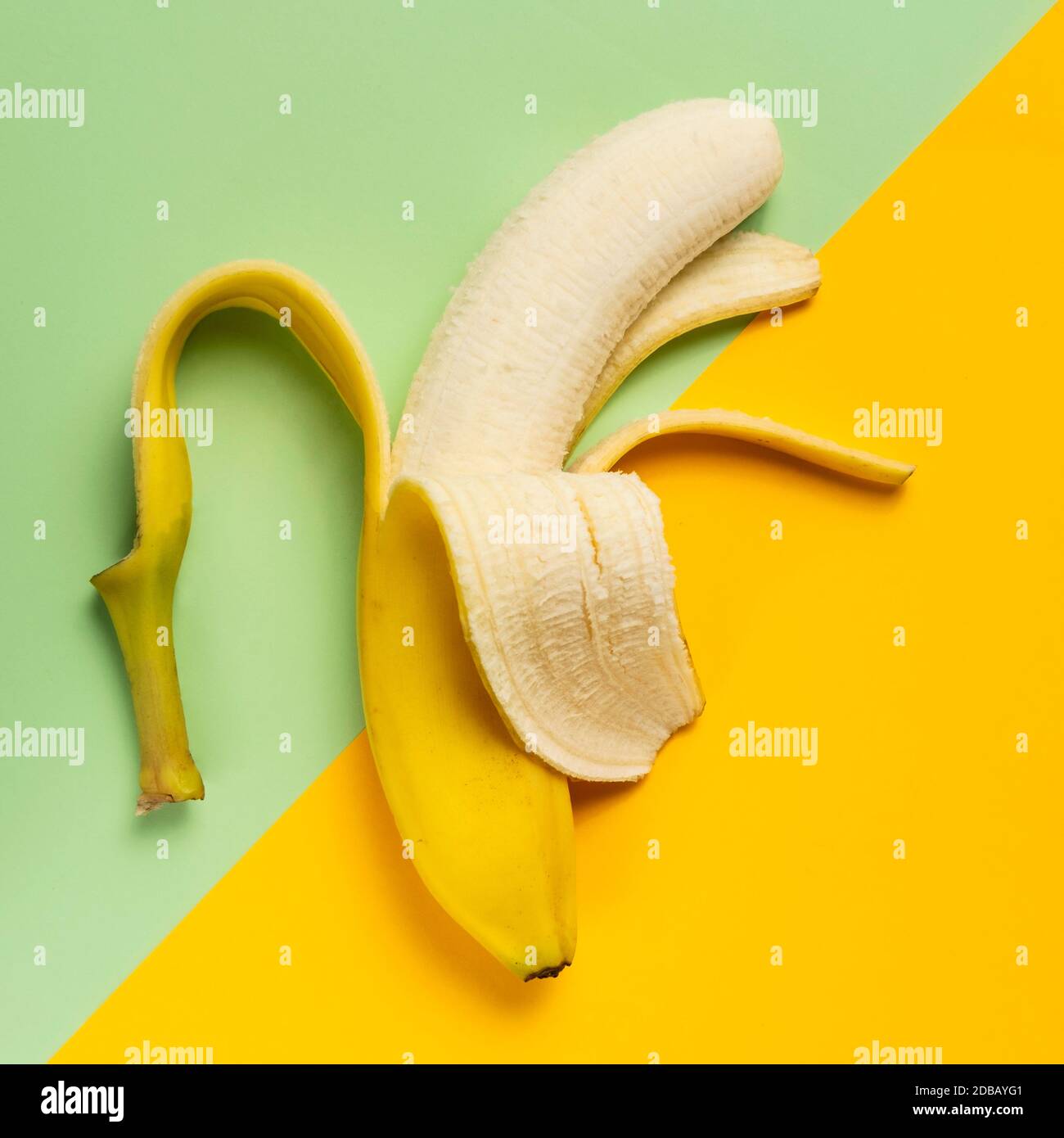 Banana pelata a metà su sfondo verde e giallo Foto Stock