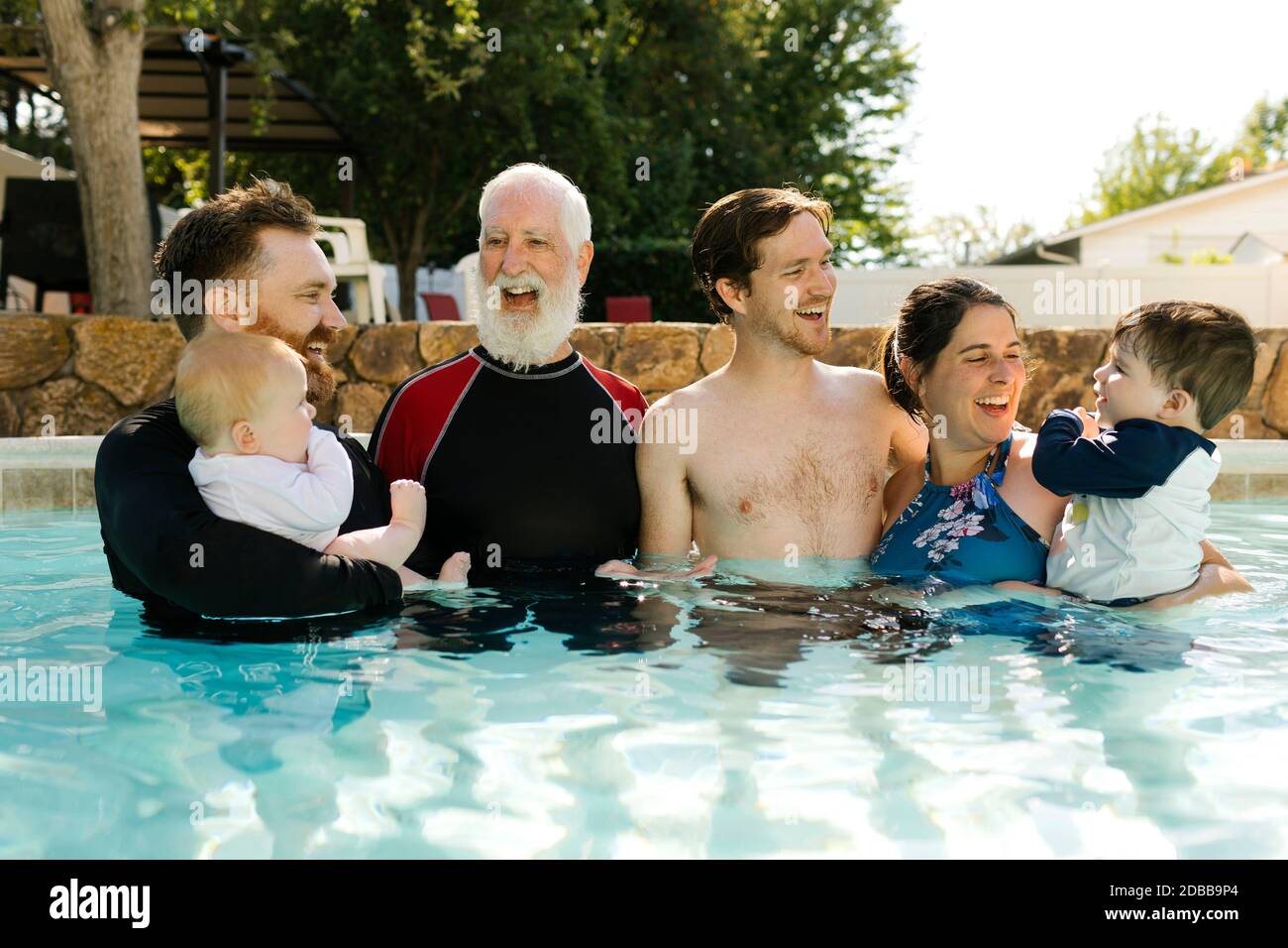 Famiglia multigenerata con bambini (2-3, 6-11 mesi) in piedi in piscina all'aperto Foto Stock