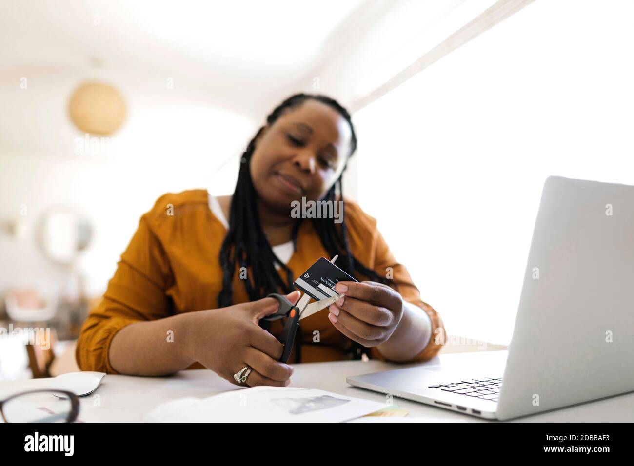 Donna tagliando carta di credito con forbici mentre lavora a casa ufficio Foto Stock
