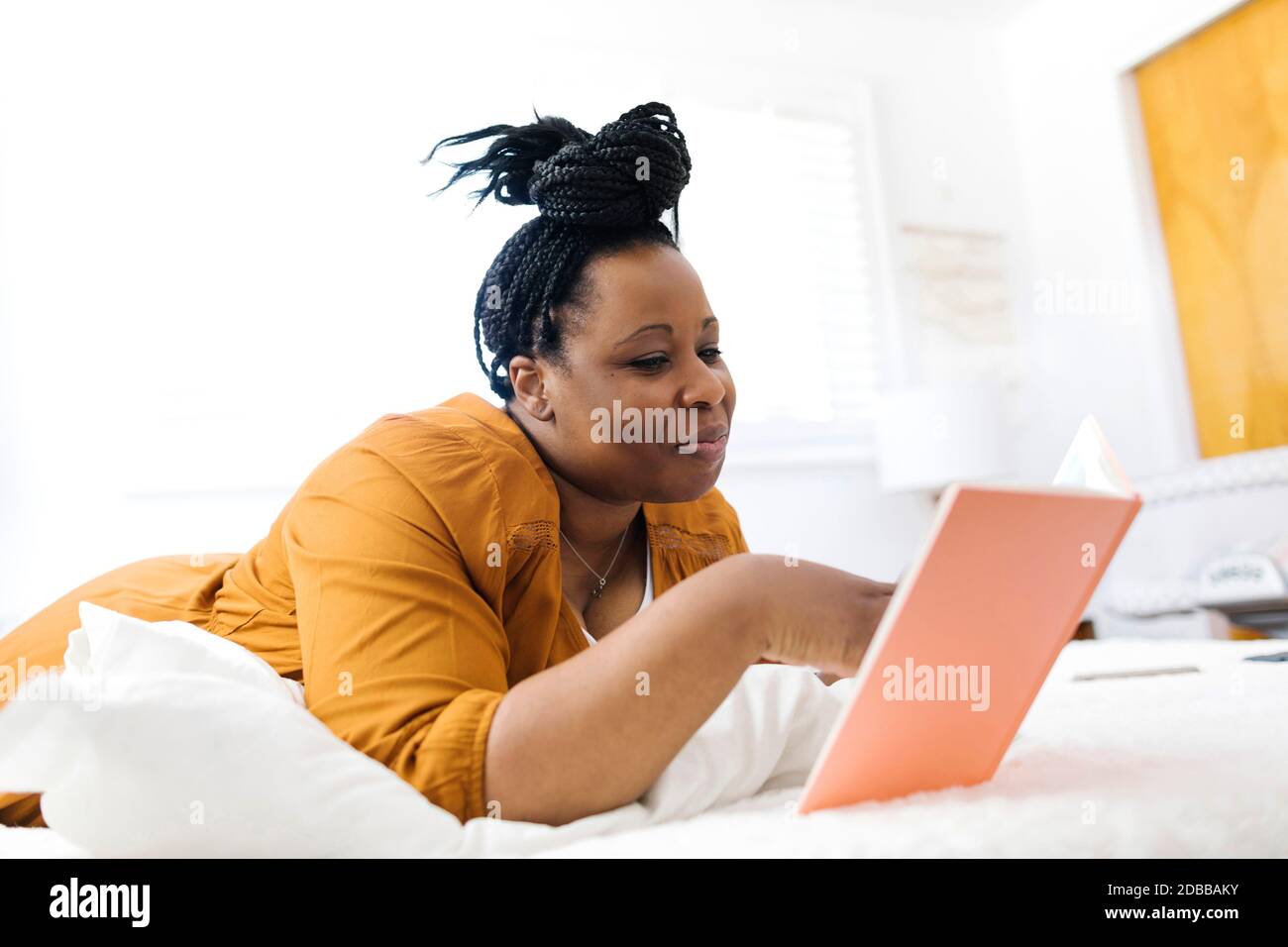 Donna sorridente sdraiata a letto e che usa la tavoletta Foto Stock