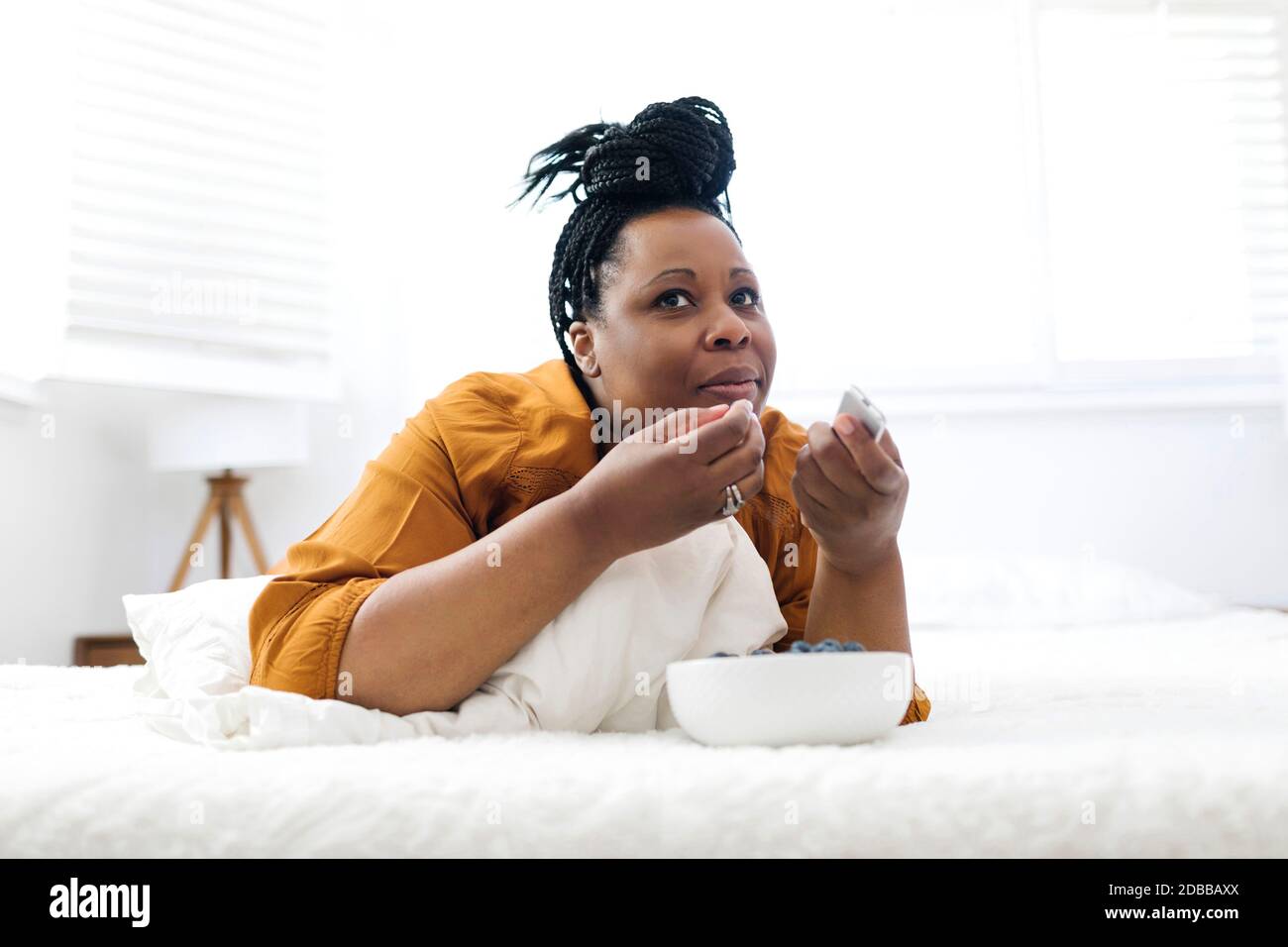 Donna sdraiata a letto, mangiando mirtilli e guardando la tv Foto Stock