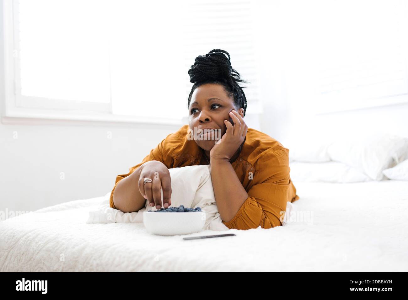 Donna sdraiata a letto, mangiando mirtilli e guardando la tv Foto Stock
