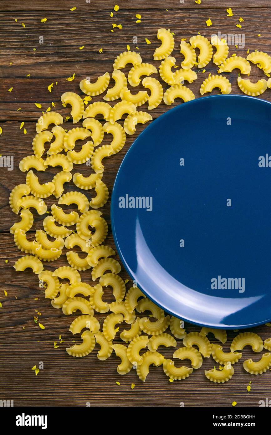 La pasta di Pene lisce a forma di un mese intorno ad un piatto blu su  sfondo di legno scuro. Viste dall'alto Foto stock - Alamy