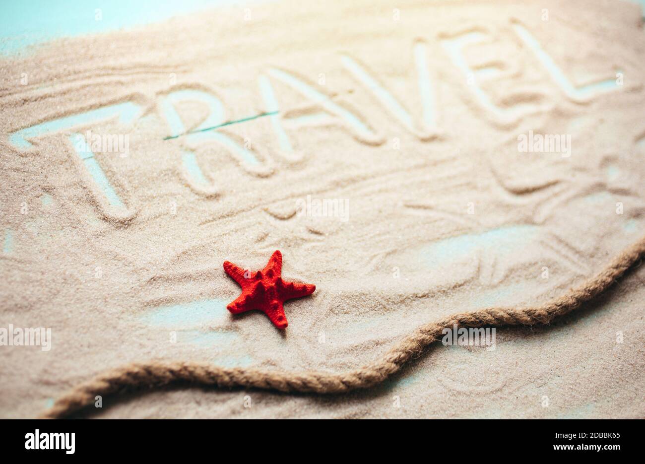 Corda per ormeggio, conchiglie e stelle marine rosse su sfondo blu tavolo in legno. L'iscrizione Travel è fatta su sabbia. Concetto di viaggio in mare. Foto Stock