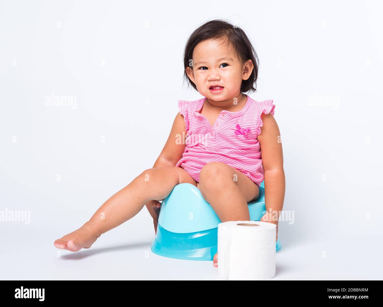 Asiatico poco cute bambino ragazza formazione di formazione a sedersi su piatto blu camera o vasino con carta igienica rotoli, studio girato isolato su bianco ba Foto Stock